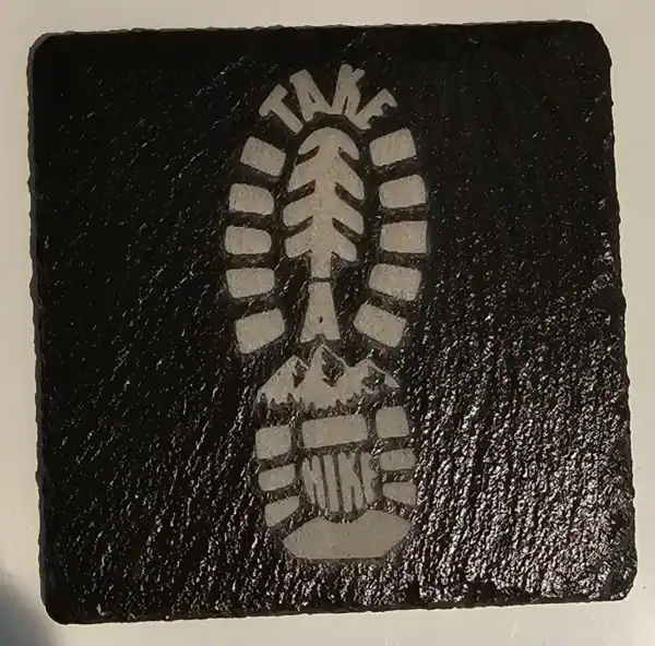 Boot print engraved on black slate coaster for outdoor enthusiasts.