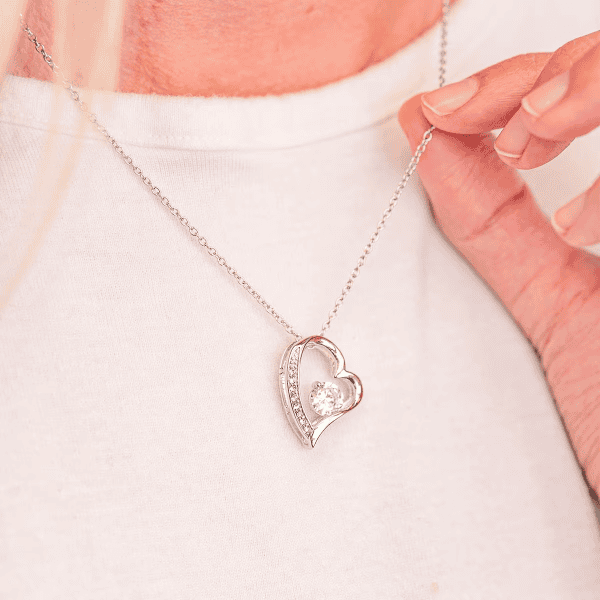 Close-up of a silver heart-shaped necklace with sparkling crystal accents, worn on a woman's neck for bridal or everyday elegance.